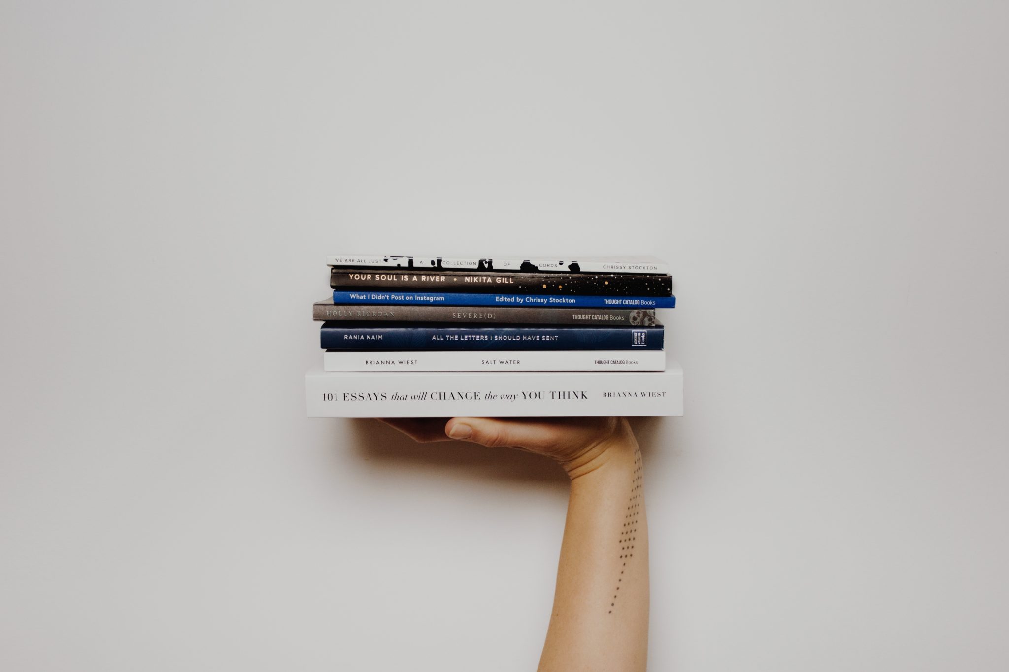 Hand holding a stack of books including 101 Essays That Will Change The Way You Think
