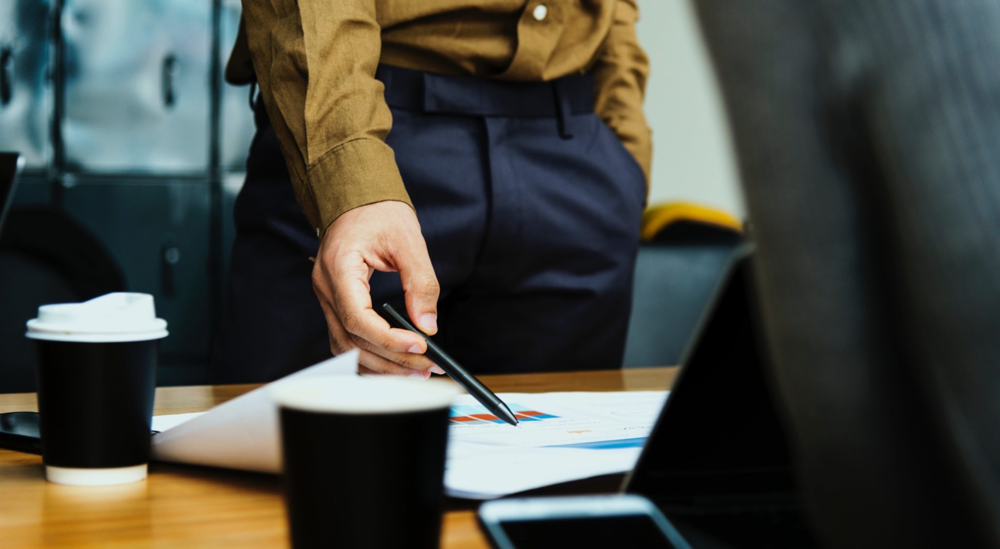 Person in tan shirt pointing a pen at printed bar charts on a desk