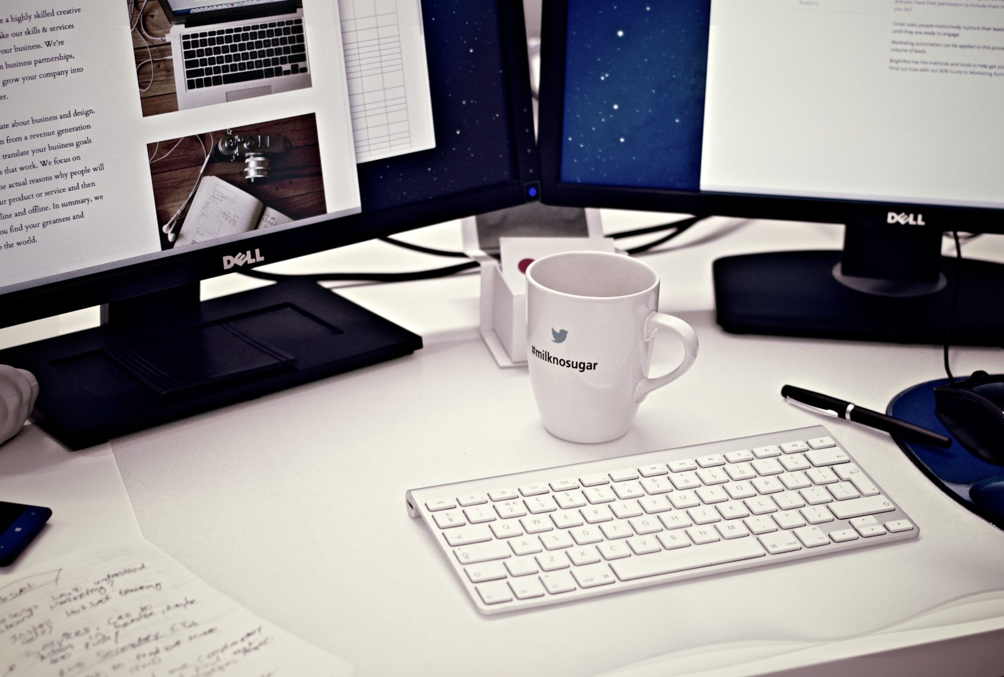 Two Dell monitors and a wireless keyboard on a desk with a coffee mug and headphones