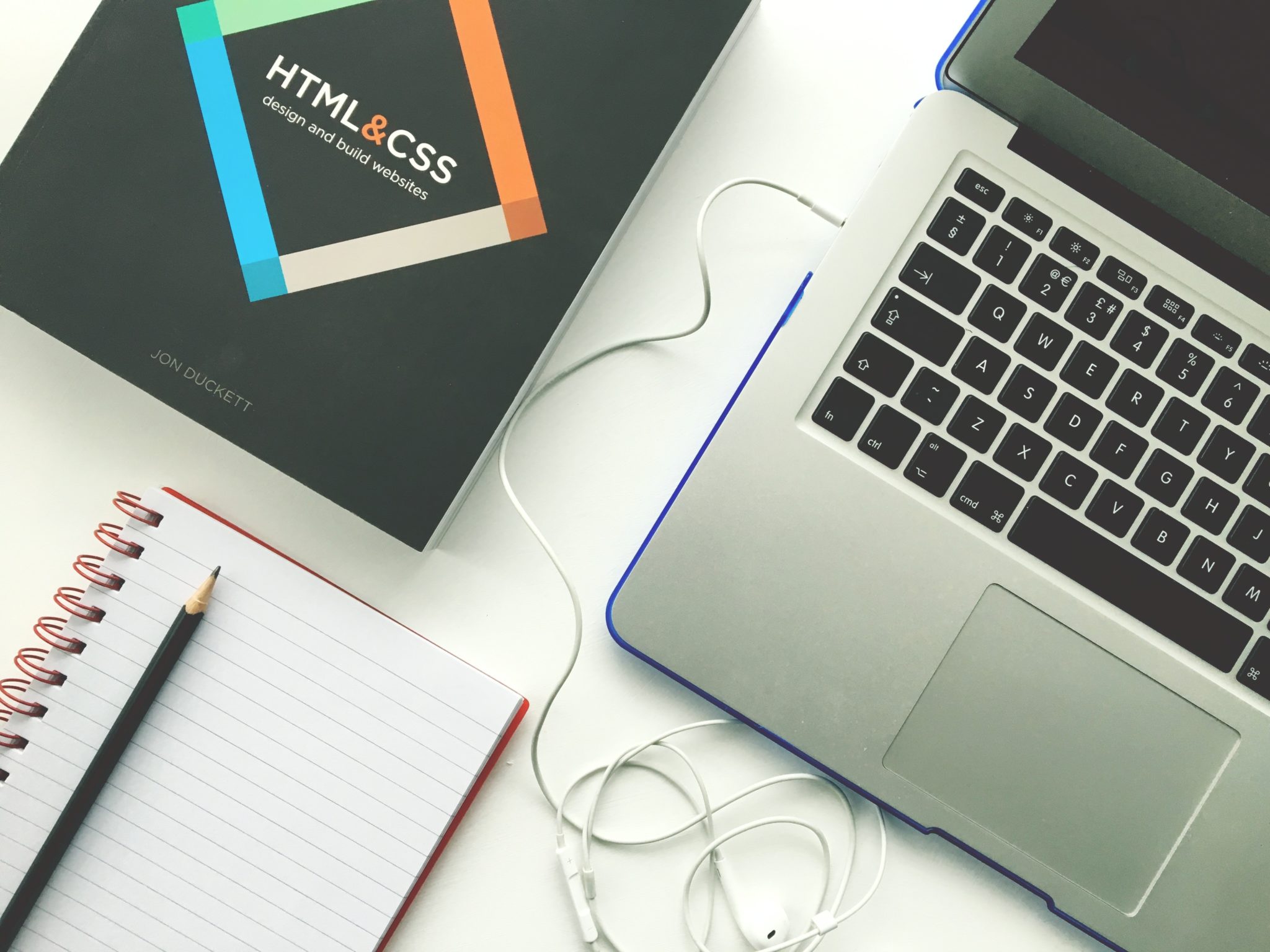HTML and CSS book by Jon Duckett next to a laptop, notebook, and earphones