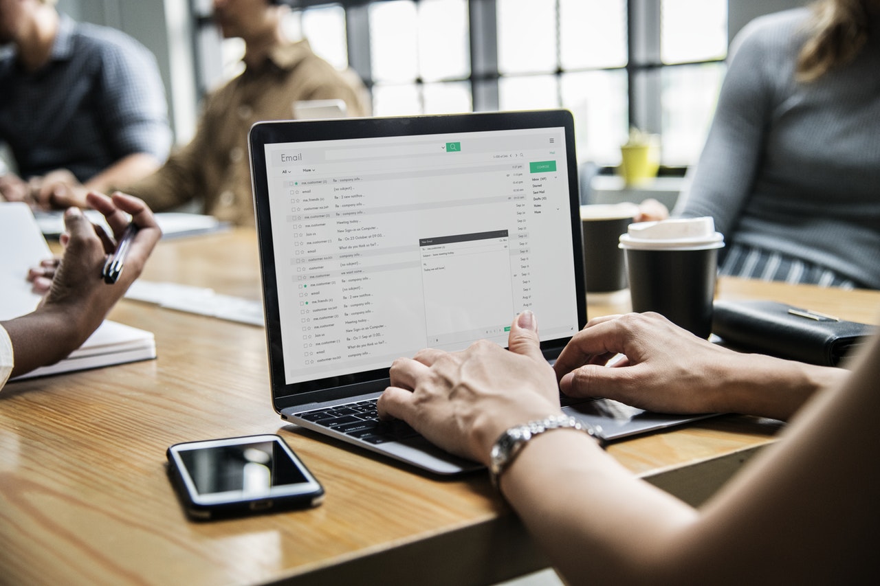 Hands typing on a laptop showing an email inbox with a meeting in progress