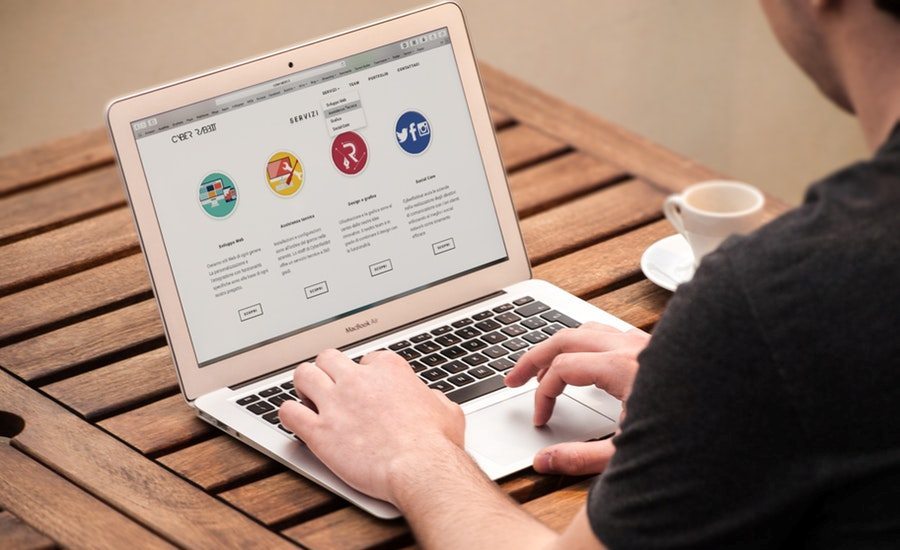 Man typing on a MacBook Air laptop displaying a web design agency homepage at a wooden table
