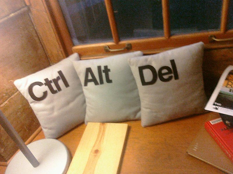 Three throw pillows printed with Ctrl, Alt, and Del on a wooden bench