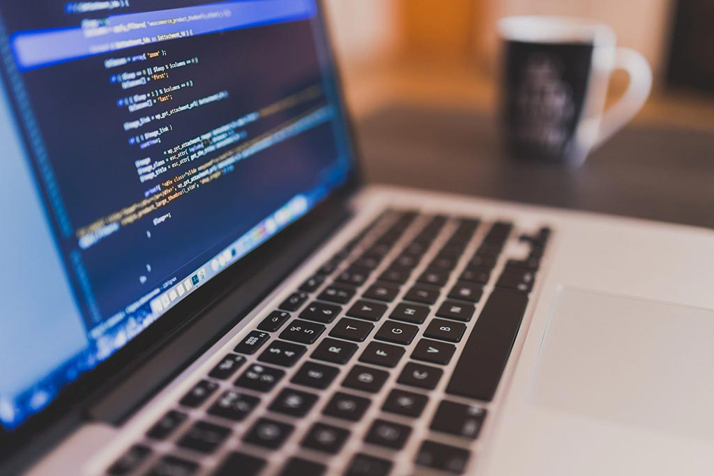 Close-up of a laptop screen showing colorful lines of code with a coffee mug