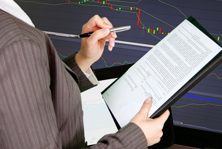 Person in suit reviewing document with stock candlestick chart in background