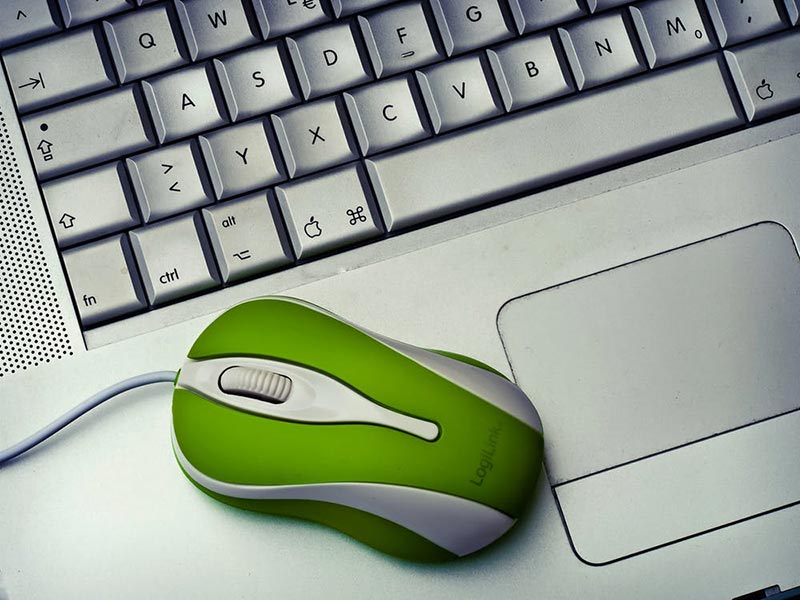 Green wired computer mouse resting on a silver laptop keyboard