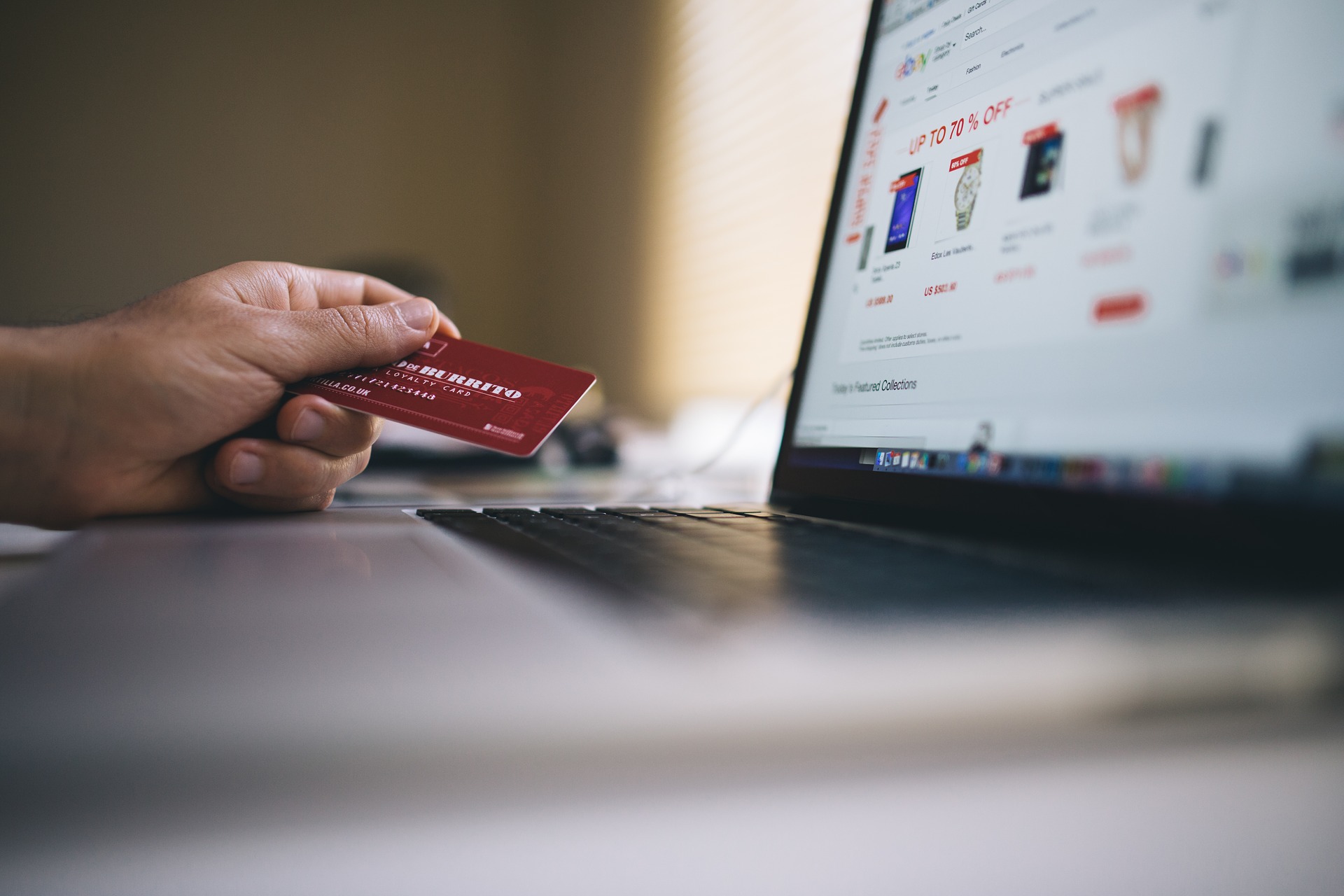 Hand holding red loyalty card next to laptop showing online store sale page