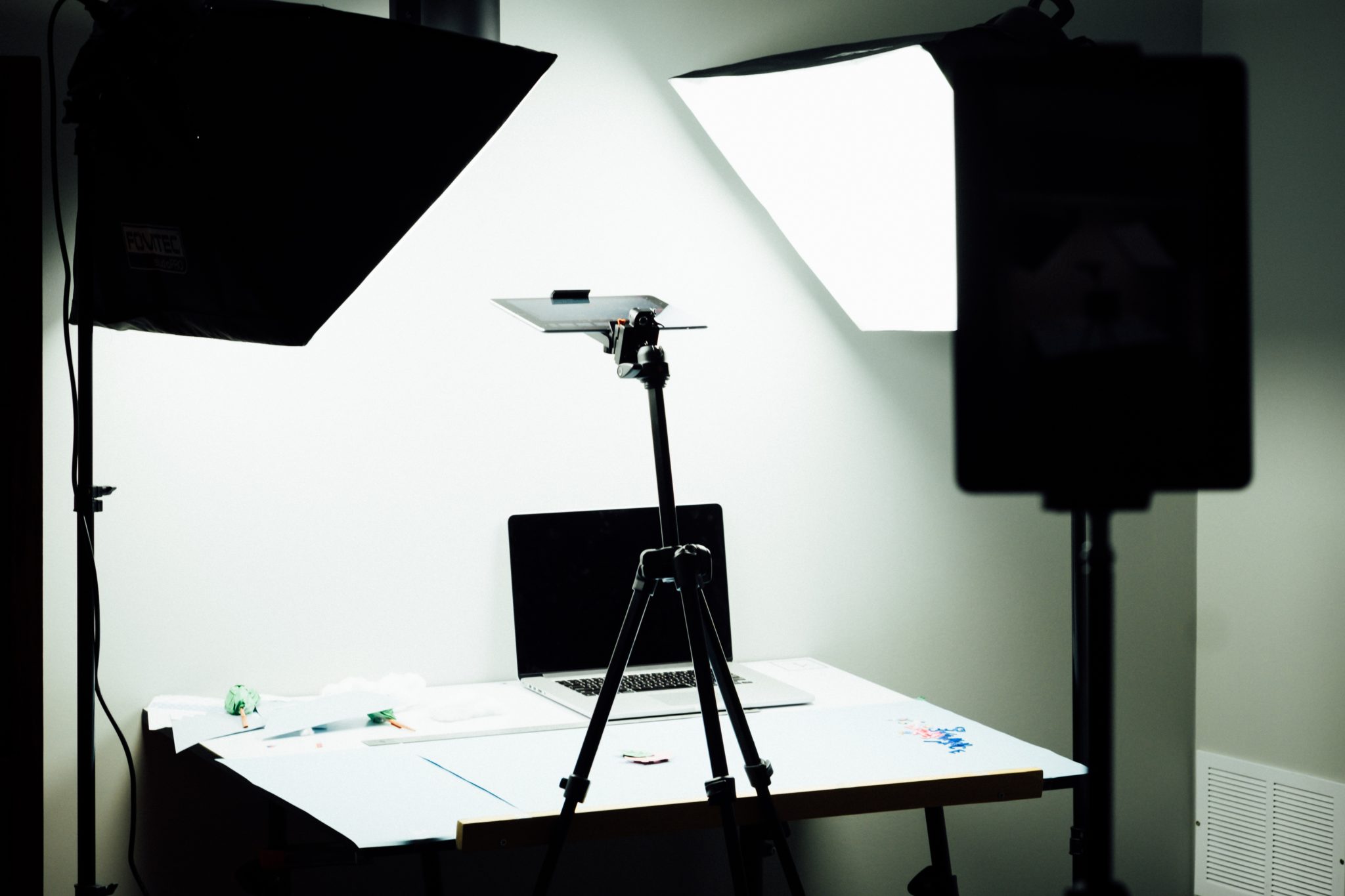 Studio photography setup with softbox lights, tripod and laptop on desk