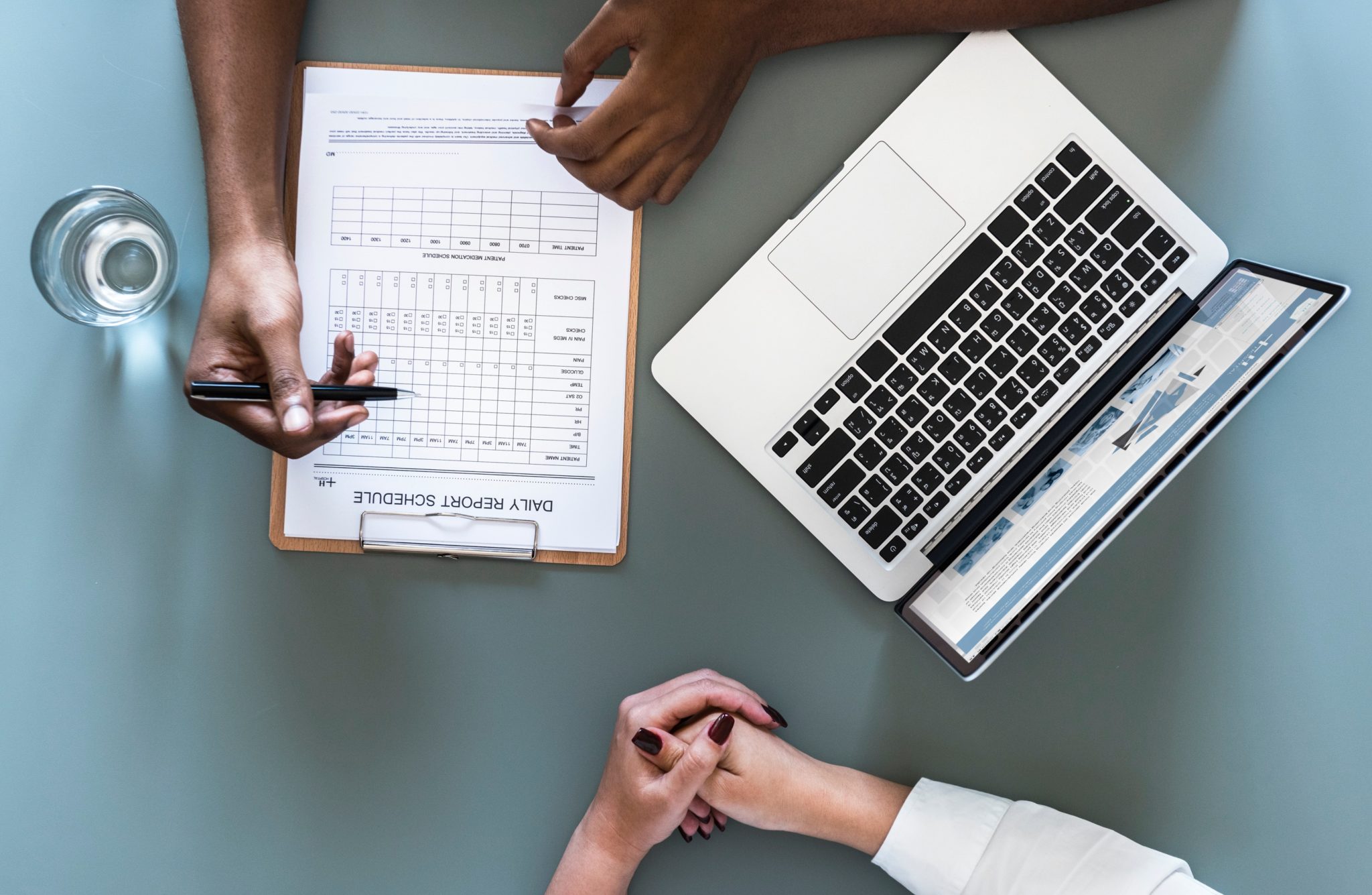 Overhead view of two people reviewing a Daily Report Schedule clipboard beside a laptop