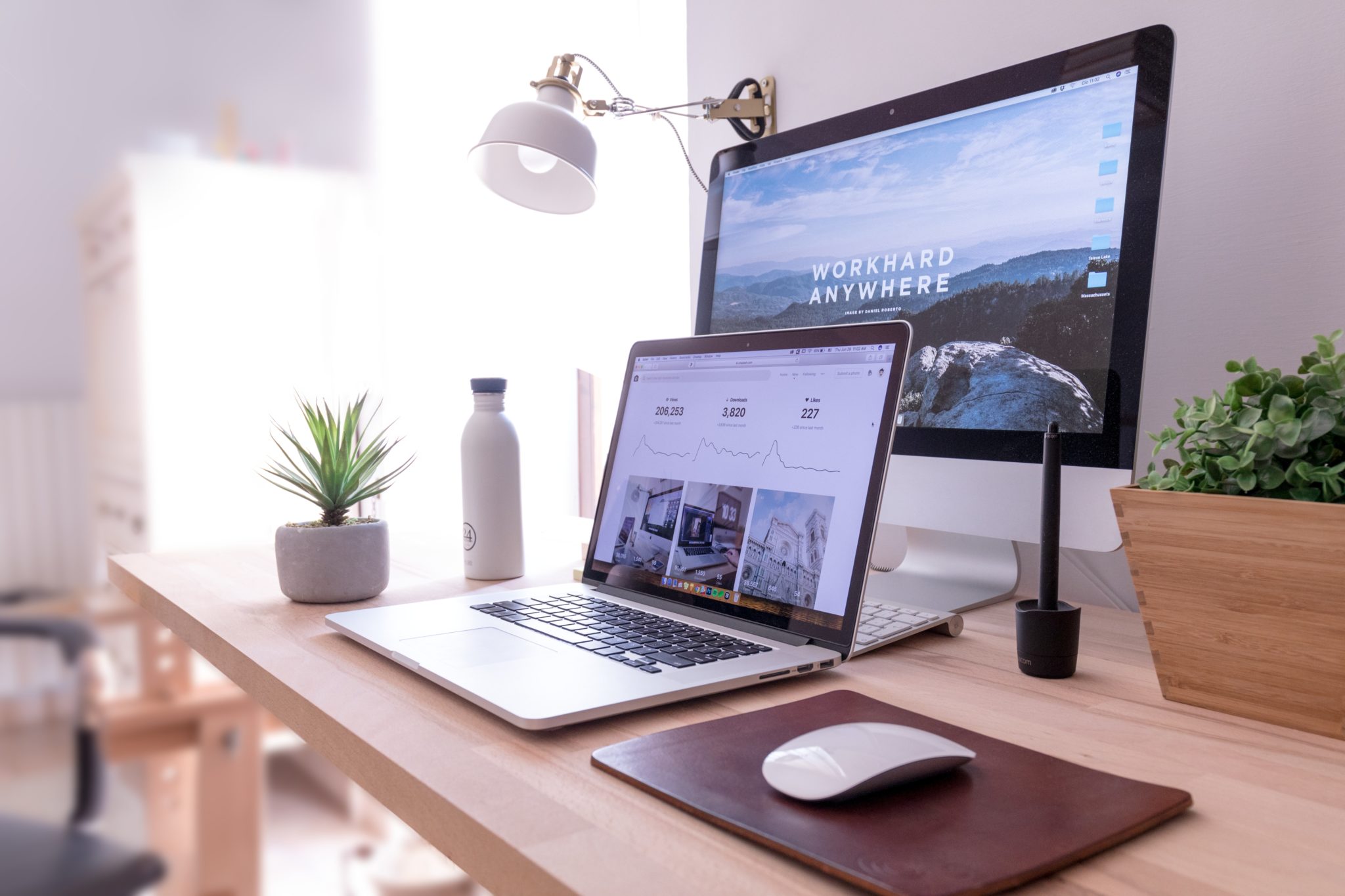 Tidy desk with a laptop and external monitor displaying a Work Hard Anywhere website