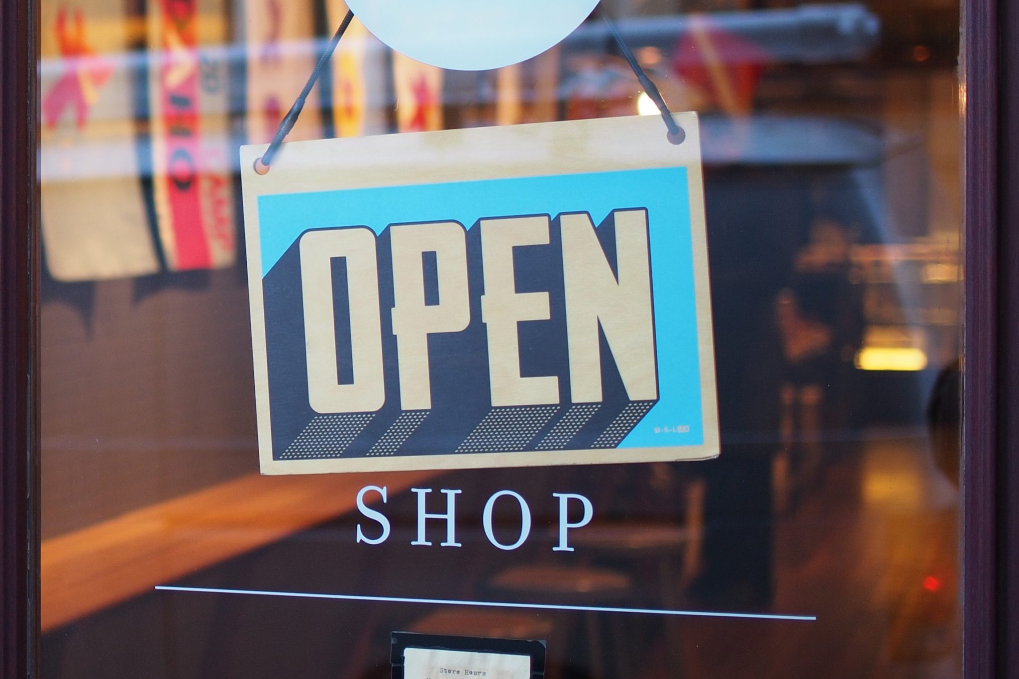 Blue and tan OPEN sign hanging in a shop window above the word SHOP