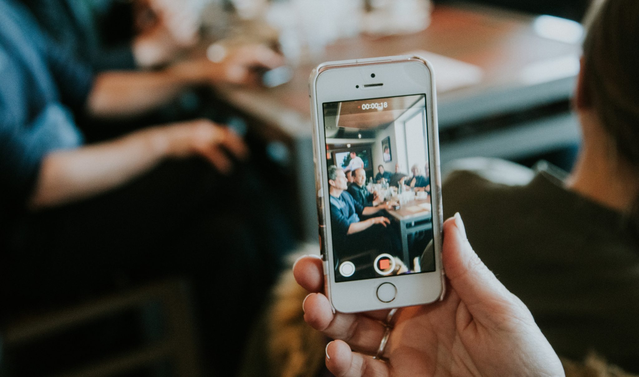 Person filming a group at a restaurant table on a smartphone