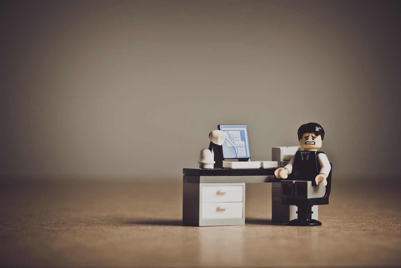 Lego minifigure with a stressed expression sitting at a tiny office desk