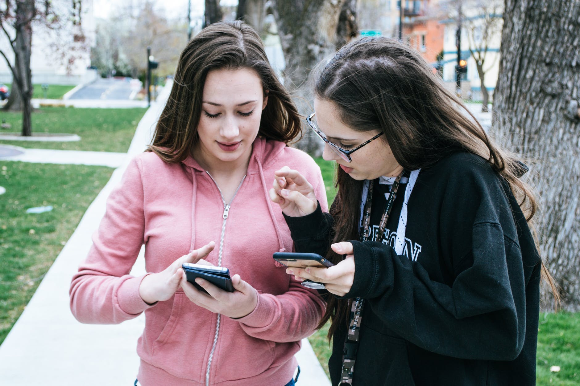 Two young women looking at smartphones together on a sidewalk